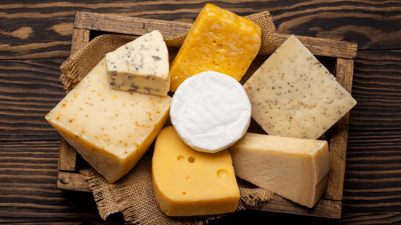 a wooden tray with assorted cheeses, including blue cheese, cheddar, colby & spiced varieties, on a rustic background