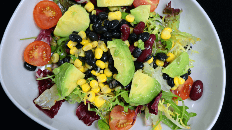 a plate full of avocado bean salad garnished with corn & cherry tomatoes