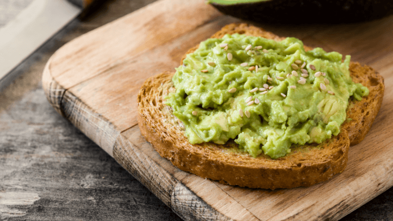 avocado toast made with whole grain bread & mashed avocado placed on a wooden board 