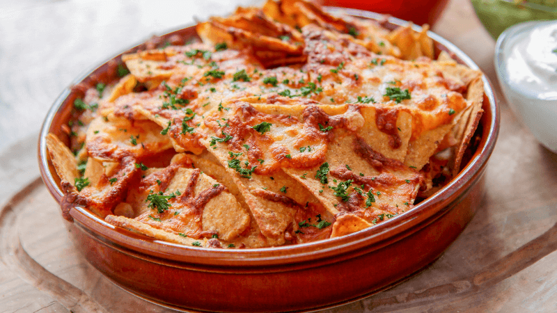 cheesy nachos baked in a brown bowl garnished with coriander