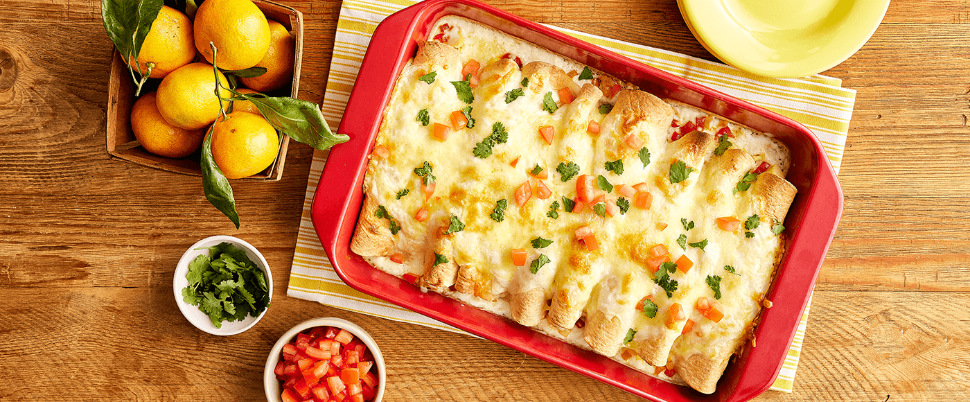 cheesy baked enchiladas in a red dish, garnished with diced tomatoes& herbs, served with salsa, cilantro & fresh limes
