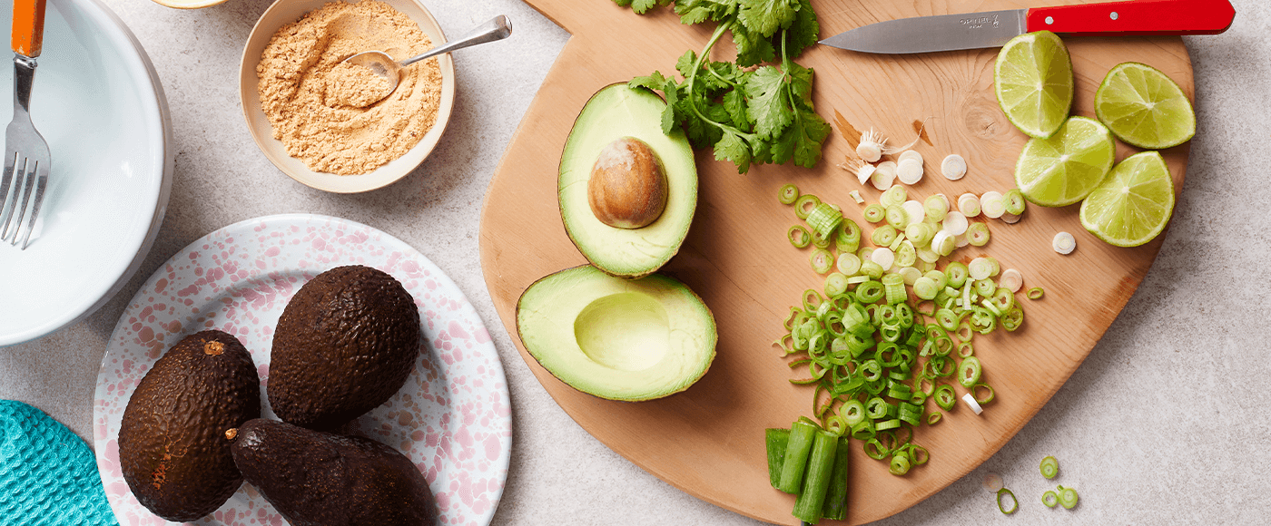 avocados, spring onion, cilantro & lime slice placed on chopping board