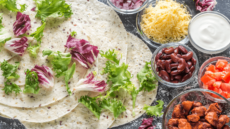 assorted enchilada ingredients such as tortillas, cheese, beans, chicken, sour cream put together