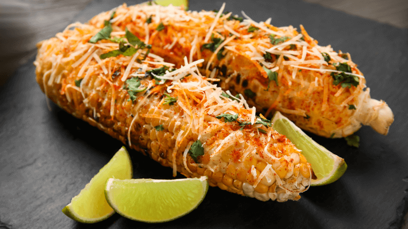 mexican street corn (elote) topped with cheese served with lime wedges