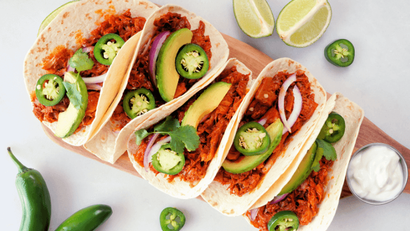 steak fajitas topped with sliced jalapenos served on a plate surrounded by lime wedges & sour cream