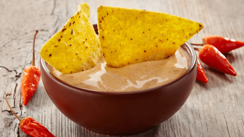 tortilla chips dipped in a queso sauce served in a bowl with red chilies around
